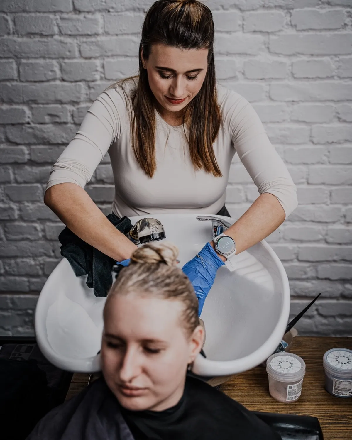 Michaela Ježová myje klientce vlasy u mycího boxu proti bílé cihlové stěně salonu